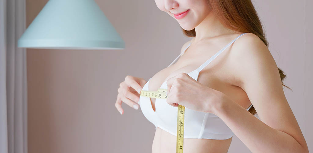 Woman in bra measuring her breasts with a tape measure. (BREAST-Q breast augmentation patient satisfaction)